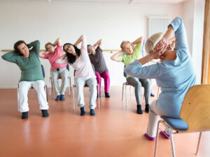 A group of women sitting in chairs doing stretching exercises