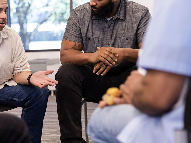 Recovery Starts When You Walk Out the Door: Why Community Is Your Lifeline 2 Two men listen to another man talk at a 12-step meeting.