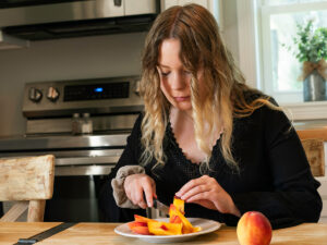 A woman sits at a table alone and slices up fresh peaches.